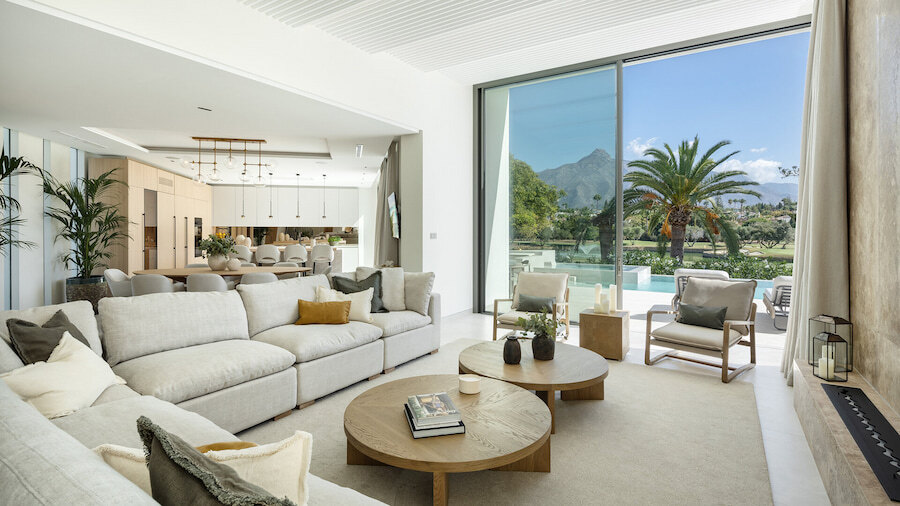 Sofisticada sala de estar de planta abierta en una villa de Marbella, con muebles de diseño, ventanas de piso a techo con vistas a la piscina, al campo de golf y a la montaña La Concha, y una conexión perfecta con las áreas de comedor y cocina.