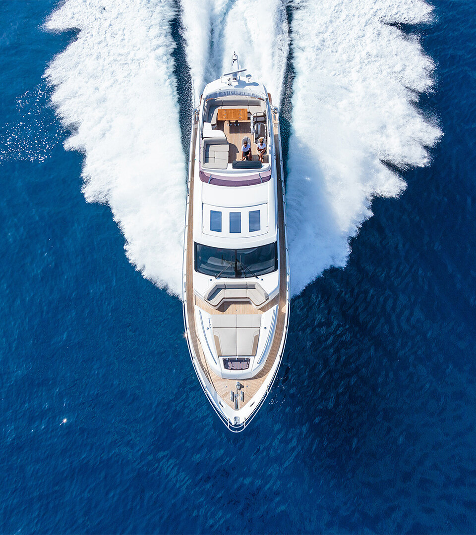Luchtfoto van een luxe jacht dat met hoge snelheid door de diepblauwe zee vaart en een witte kielzog achterlaat.
