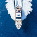Aerial view of a luxury yacht speeding through deep blue sea, leaving a white wake behind.