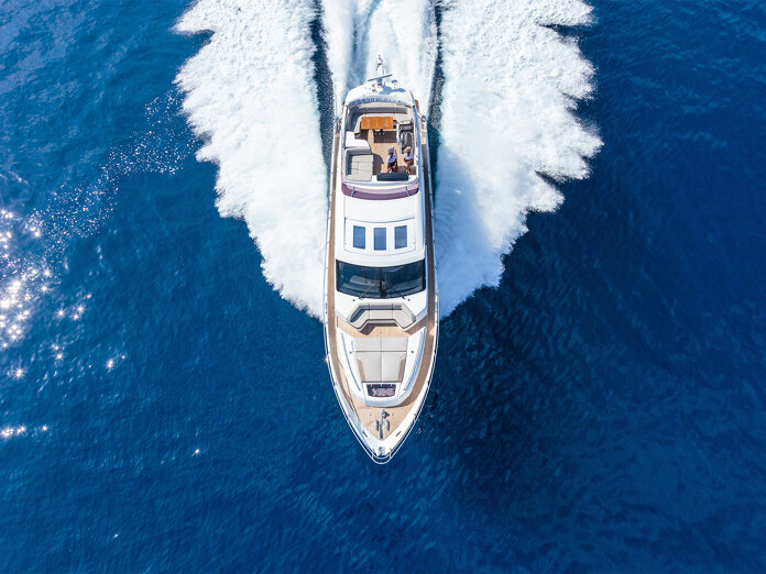 Luchtfoto van een luxe jacht dat met hoge snelheid door de diepblauwe zee vaart en een witte kielzog achterlaat.