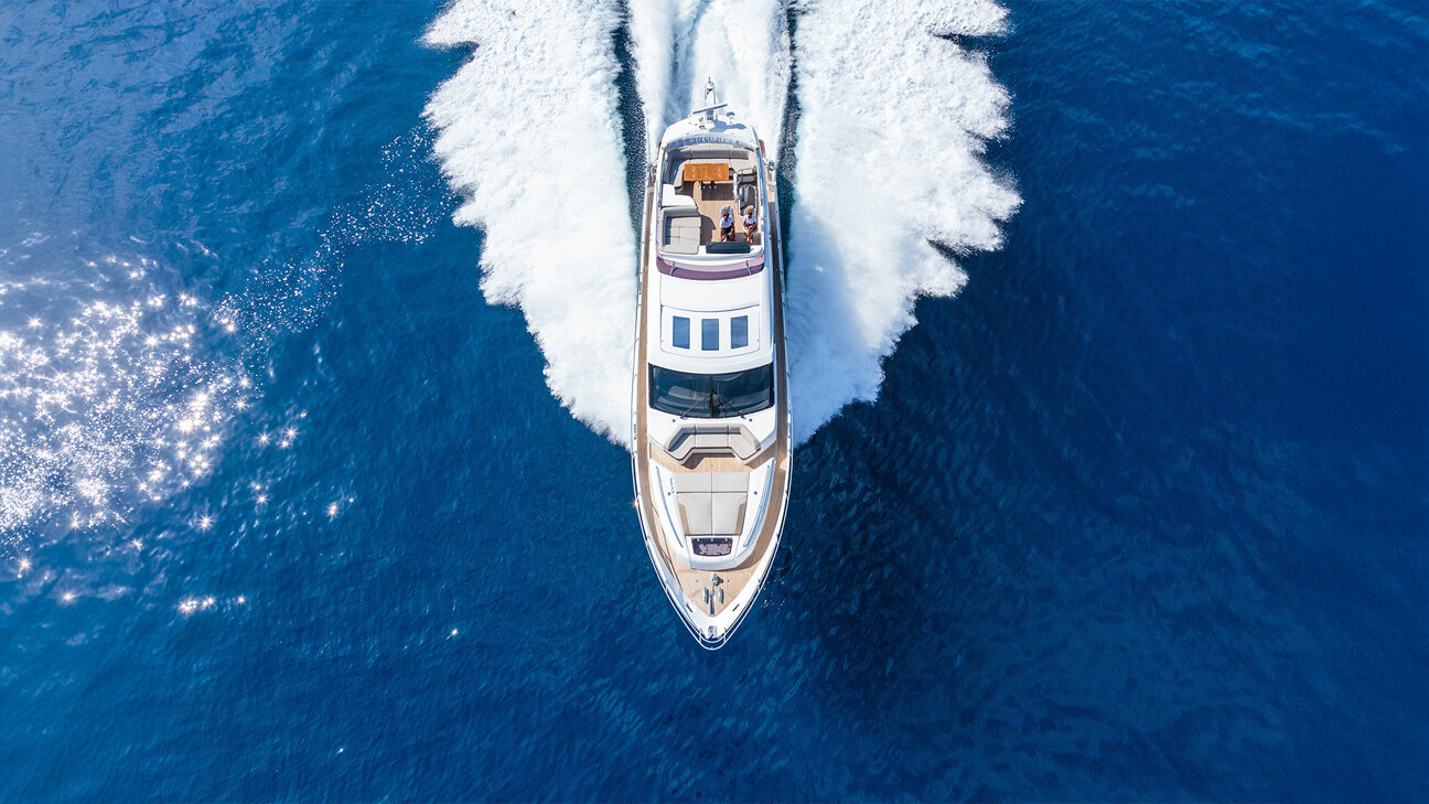 Private Yachtcharter und Segeln in Marbella. Luftaufnahme einer Luxusyacht, die mit hoher Geschwindigkeit durch das tiefblaue Meer fährt und eine weiße Heckwelle hinter sich lässt.