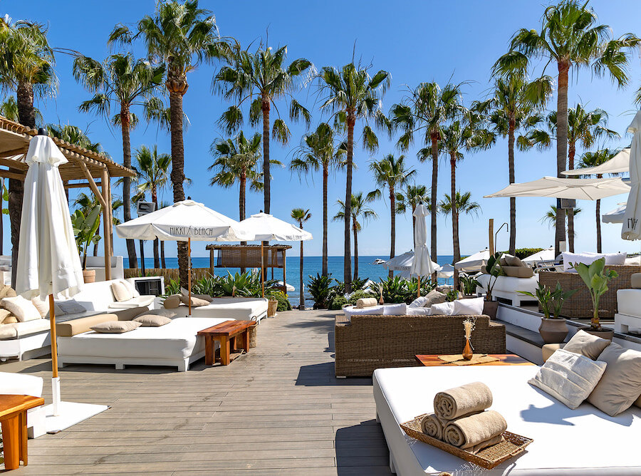 Luxe beachclub in Marbella met ligbedden, parasols, palmbomen en uitzicht op zee.