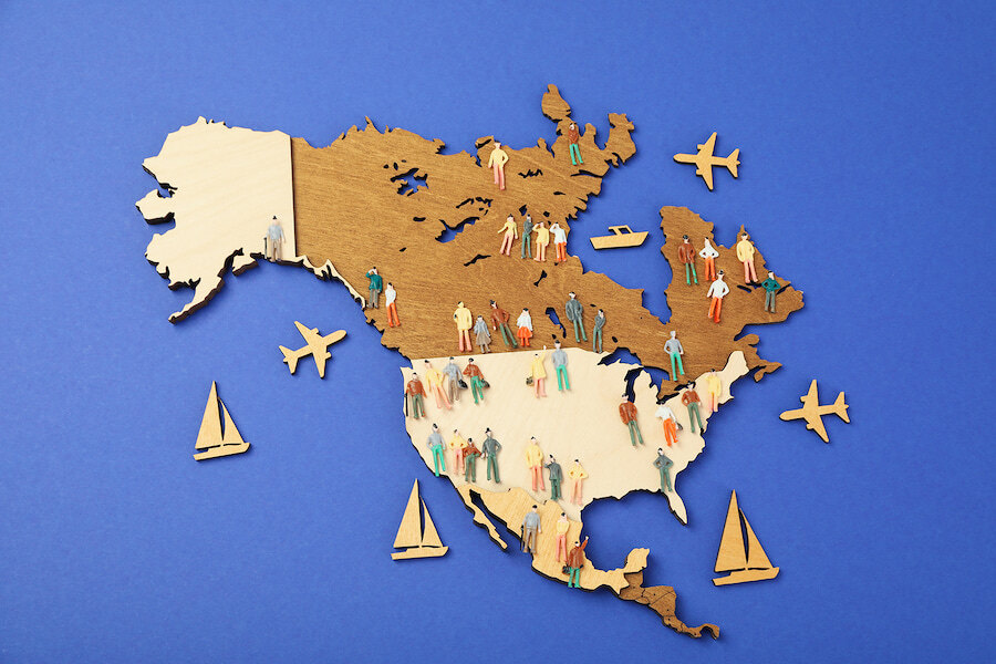 Carte en bois de l’Amérique du Nord avec des figurines miniatures, des avions et des bateaux symbolisant les voyages et les personnes.