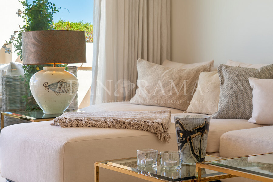 Elegantes Wohnzimmer mit beigem Sofa, strukturierten Kissen, dekorativer Lampe und Glastisch. Tipps für Luxusimmobilien