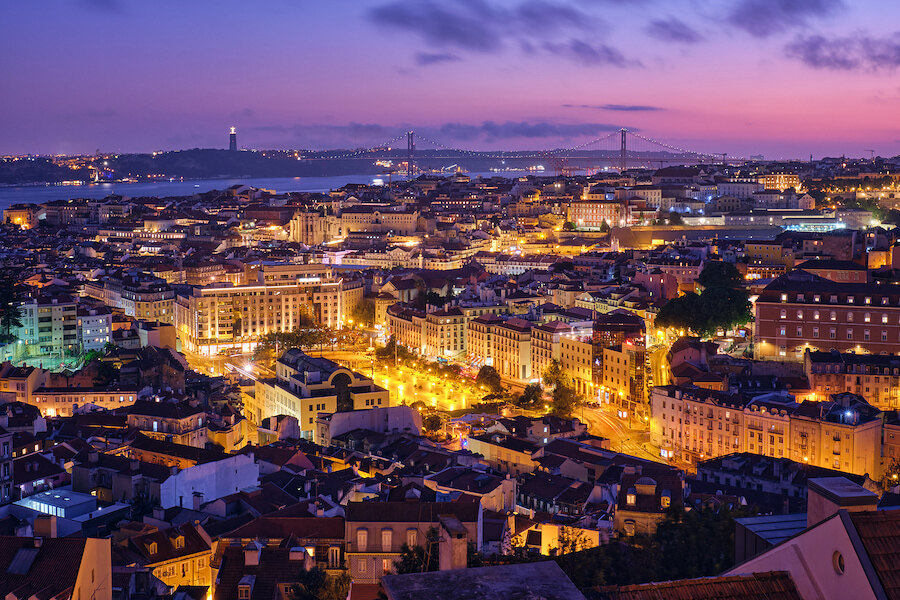Vue panoramique de Lisbonne au crépuscule avec les lumières de la ville, les toits et le pont du 25 Avril en arrière-plan.