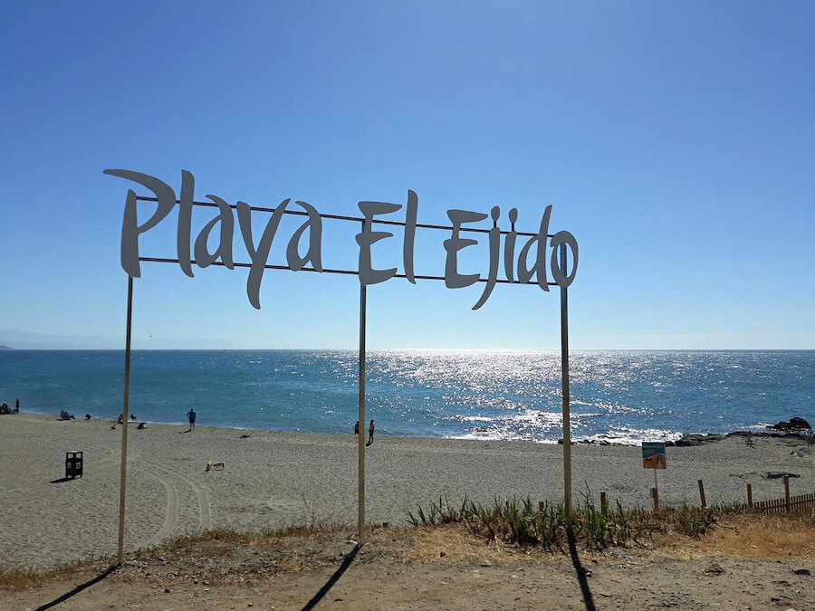 Vue de Playa El Ejido à Marbella, avec son panneau de plage au premier plan et la mer Méditerranée scintillant sous le soleil.