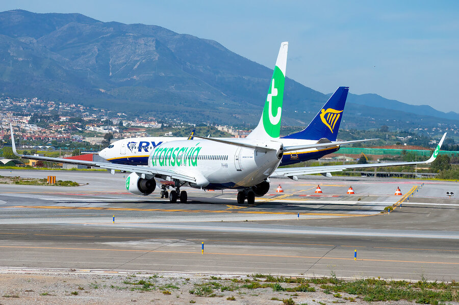 Transavia and Ryanair airplanes taxiing on the runway at Málaga Airport, with mountains in the background.