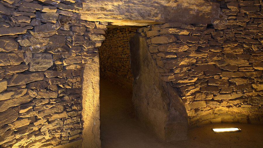 Interieur van de dolmen El Romeral in Antequera, Málaga, met zorgvuldig opeengestapelde stenen muren, smalle doorgangen en warme verlichting die de textuur van de rotsen benadrukt.