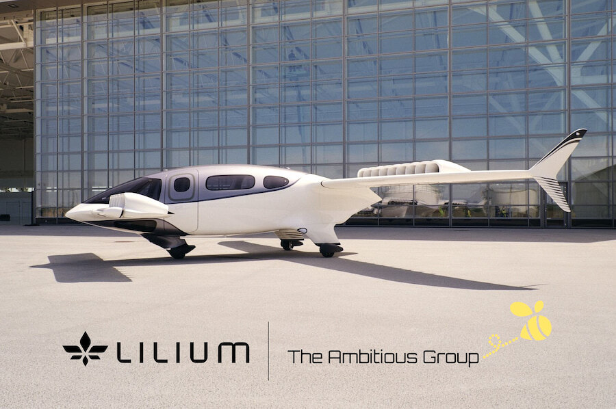 Lilium electric vertical take-off and landing (eVTOL) aircraft parked outside a large glass hangar, with Lilium and The Ambitious Group logos displayed in the foreground.