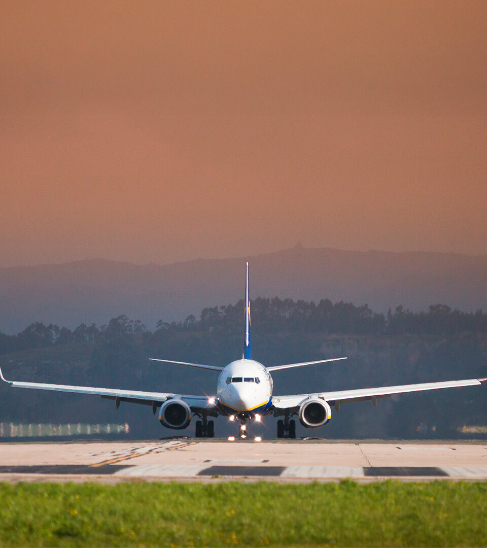 Front view of a commercial airplane on the runway preparing for takeoff, with an orange sky and distant hills in the background.