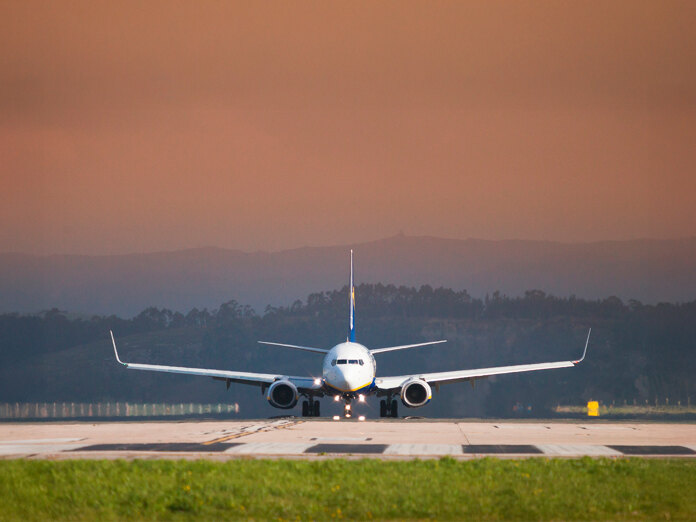 Front view of a commercial airplane on the runway preparing for takeoff, with an orange sky and distant hills in the background.