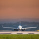 Front view of a commercial airplane on the runway preparing for takeoff, with an orange sky and distant hills in the background.