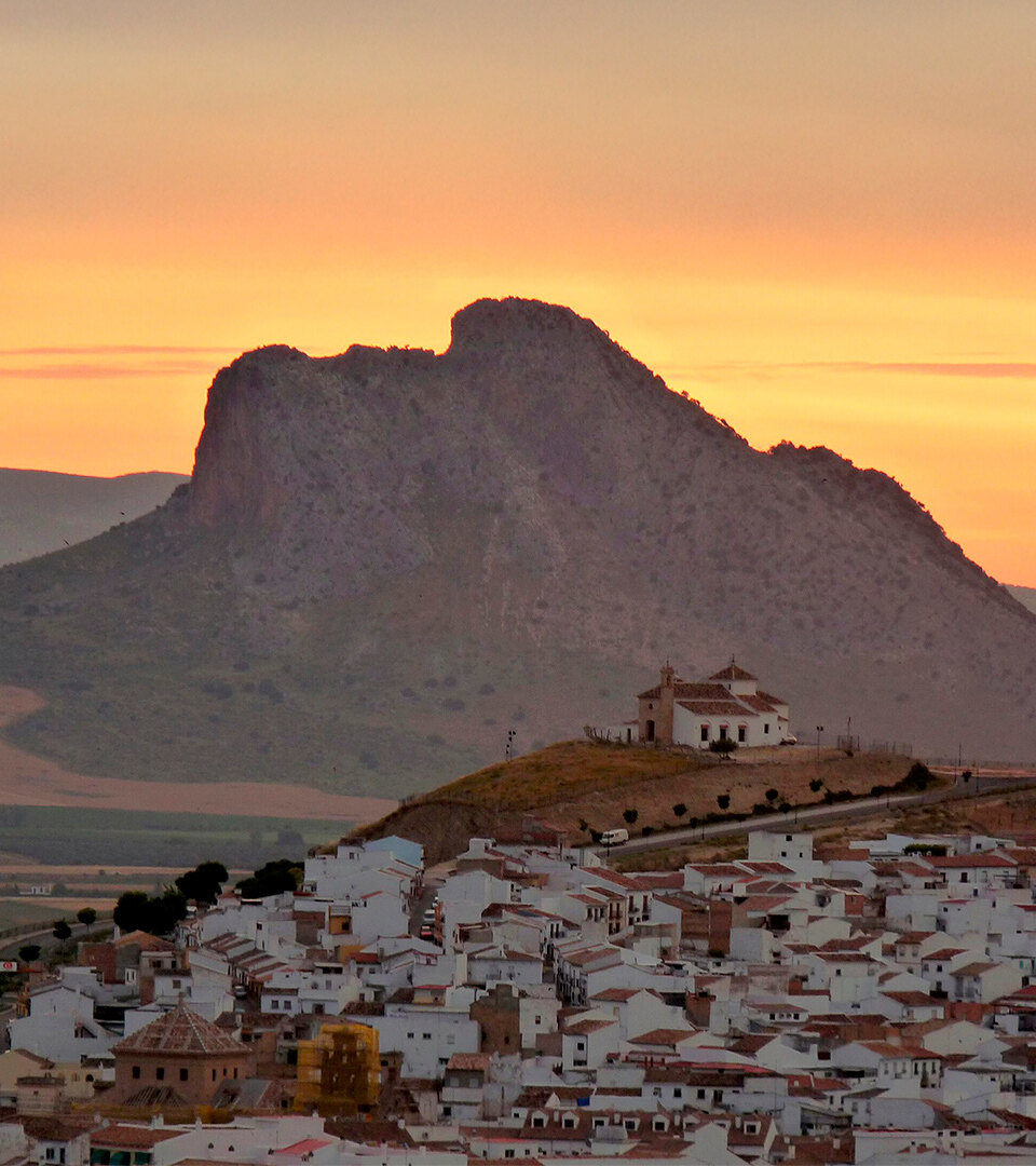 Zonsondergang boven de Peña de los Enamorados in Antequera, met het menselijke gezicht van de rots en het witgekalkte stadje op de voorgrond.
