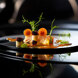 Michelin-Star Magic: Fine Dining Experiences in Marbella. A haute cuisine dish with an artistic and minimalist presentation, composed of salmon, spherules, green sprouts, and sauces, served on a glossy black plate with elegant highlights.