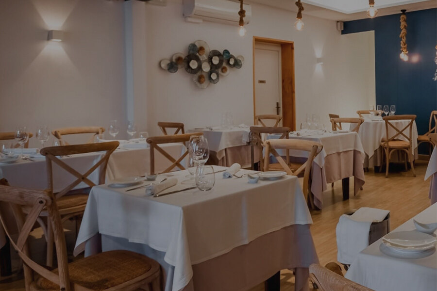 Interior of an elegant restaurant with tables dressed in white tablecloths, wine glasses, and wooden chairs, in a cosy and well-lit atmosphere.